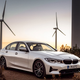 A photo of a BMW 330e sedan with wind turbines in the background.